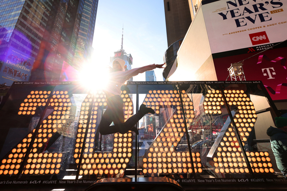  31일 밤 새해맞이 축하행사에 쓰일 2022년 숫자 전광판이 맨해튼 타임스스퀘어에 전시돼 있는 가운데, 한 여성이 점프하며 기념사진을 찍고 있다. [로이터]