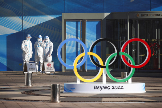방호복을 착용한 ‘2022년 베이징 겨울 올림픽’ 관계자들이 중국 베이징 내셔널 스타디움에 설치된 오륜기 옆에 서 있다.  [사진 로이터] 