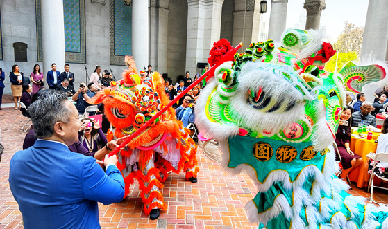 12일 존 이 LA시의원(왼쪽)이 LA시청에서 열린 아태 문화유산의 달 기념식에서 공연을 펼친 중국 사자춤 무용수에게 안녕을 기원하는 생야채를 전달하고 있다. 김상진 기자