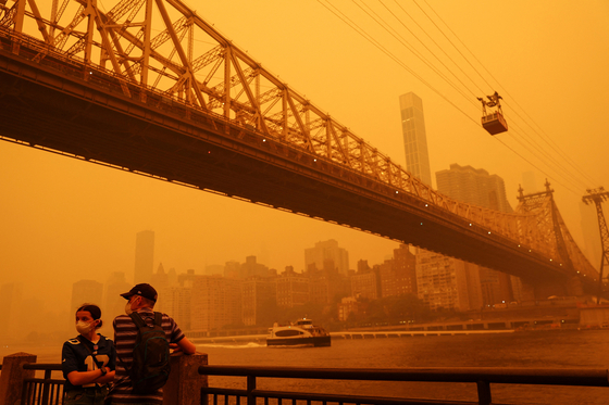 캐나다에서 번진 산불 연기의 여파로 7일 뉴욕시 하늘이 뿌연 오렌지색으로 변한 가운데, 마스크를 쓴 시민들이 루스벨트아일랜드에서 이스트리버와 흐려진 스카이라인을 바라보고 있다. [로이터]