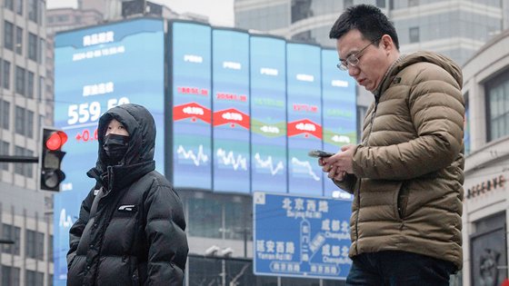 지난 6일 중국 상하이 거리에서 사람들이 금융 정보를 보여주는 대형 전광판 앞을 지나는 모습. EPA=연합뉴스