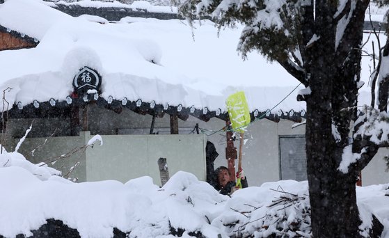 지난 21일 강원 강릉시 성산면 대관령 기슭의 한 마을에서 주민이 지붕에 쌓인 눈을 치우고 있다. [연합뉴스]