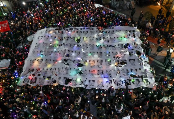 12일 오후 서울 영등포구 국민의힘 당 사무실 앞에서 열린 윤석열 대통령 탄핵 촉구 촛불 집회 행진에 참석한 시민들이 윤 대통령의 탄핵소추안 투표에 불참한 국민의힘 의원들을 규탄하는 현수막을 찢고 있다. 연합뉴스