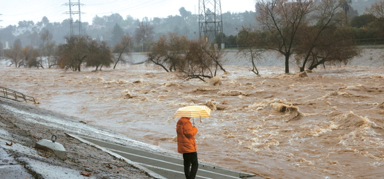가주 전역에 이틀째 쏟아진 폭우로 피해가 잇따르고 있다. 5일 우산을 쓴 행인이 불어난 LA강을 바라보고 있다.  [로이터] 